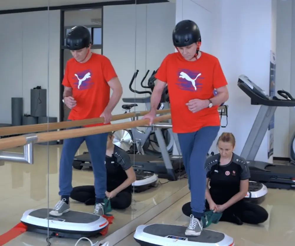 Mężczyzna w kasku poddawany jest rehabilitacji na platformie wibracyjnej PowerBoard.